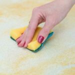hand using scrubber sponge to clean grease from white surface