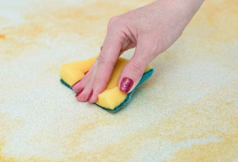 hand using scrubber sponge to clean grease from white surface