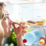 Close up of a woman looking into a fridge while holding her nose