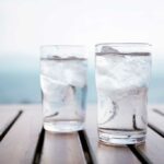 2 glasses of iced water on a slatted wooden table in front of an ocean view