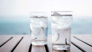 2 glasses of iced water on a slatted wooden table in front of an ocean view