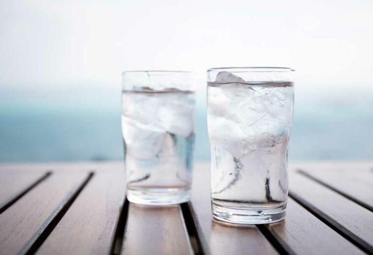 2 glasses of iced water on a slatted wooden table in front of an ocean view