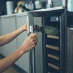 Closeup of hands opening a wine fridge and removing a bottle of wine.