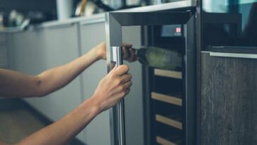 Closeup of hands opening a wine fridge and removing a bottle of wine.
