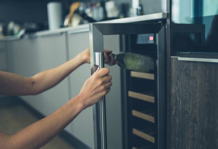 Closeup of hands opening a wine fridge and removing a bottle of wine.