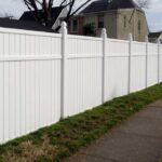 White vinyl privacy fence lining a yard next to a sidewalk.
