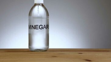 Generic bottle of vinegar sitting on a wood surface against a grey background.