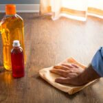Person cleaning a floor with 2 bottles of cleaner and a yellow cloth