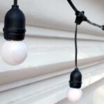 Black and white string lights with round blubs against white house siding