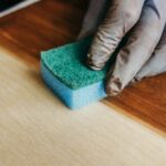 Gloved hand staining wood with a sponge