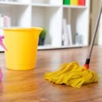 Yellow mop bucket, mop and pink spray bottle on a wood laminate floor