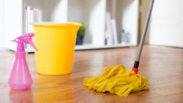 Yellow mop bucket, mop and pink spray bottle on a wood laminate floor