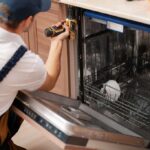 Repair man removing screws that are holding in the dishwasher
