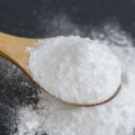 Baking soda spilling onto a dark surface from a wooden spoon