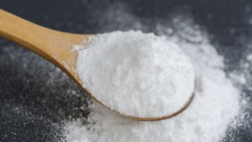 Baking soda spilling onto a dark surface from a wooden spoon