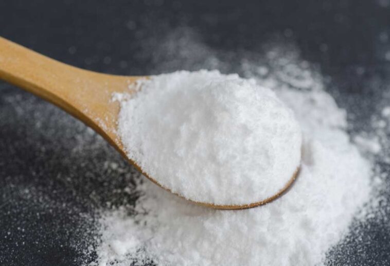 Baking soda spilling onto a dark surface from a wooden spoon