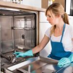 Woman kneeling in front of an open dishwasher cleaning the inside