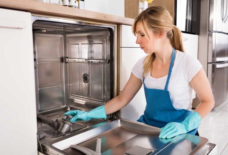 Woman kneeling in front of an open dishwasher cleaning the inside