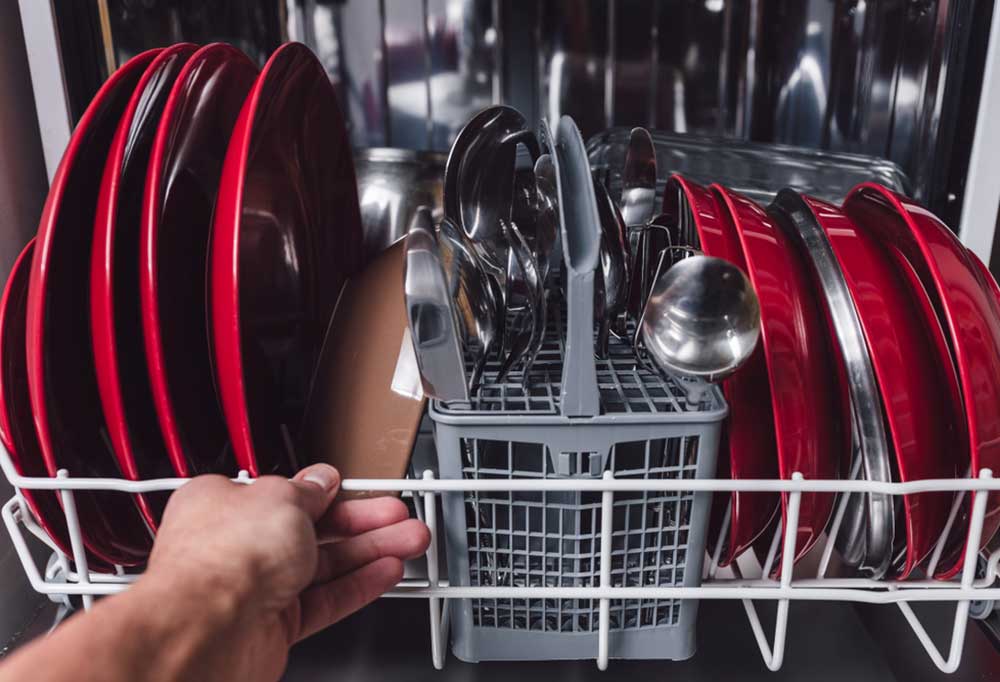 Close up of a dishwasher full of red dished and stainless steel utensils.