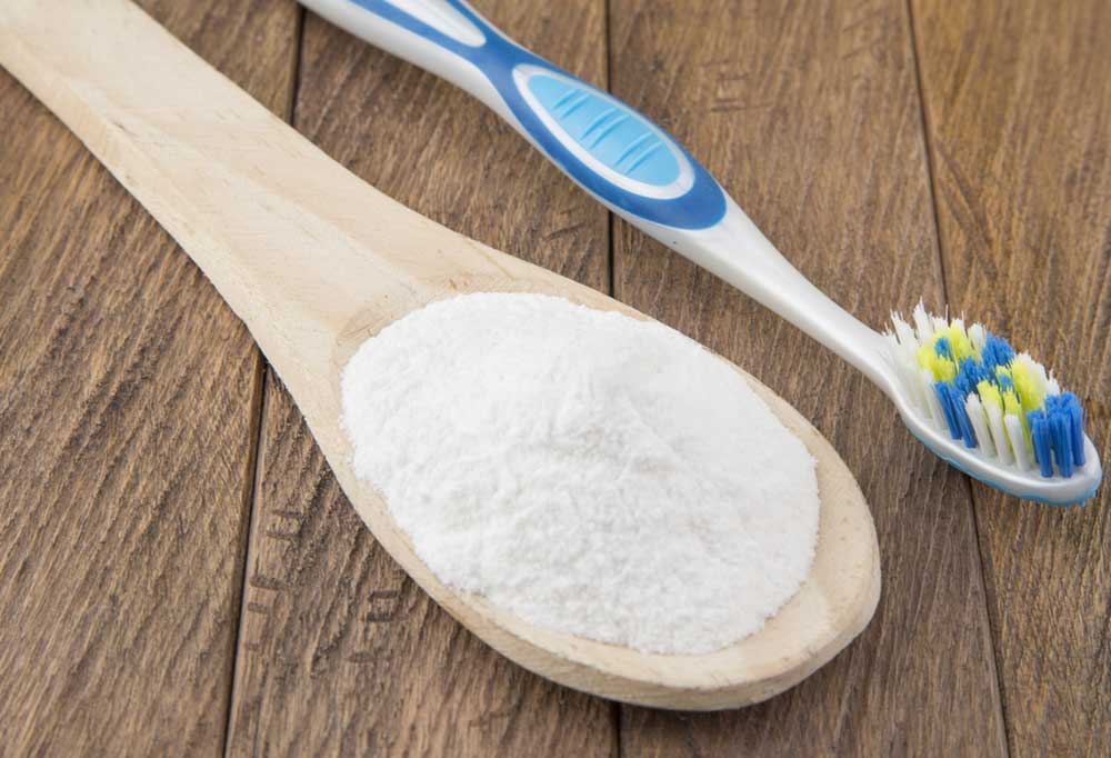 Wooden spoon full of baking soda and a toothbrush laying on a wooden table