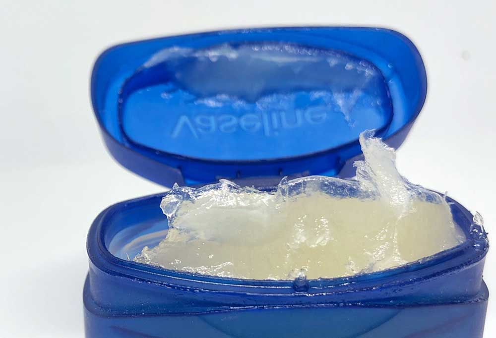 Close up of the open blue lid of a jar of Petroleum Jelly on a white background