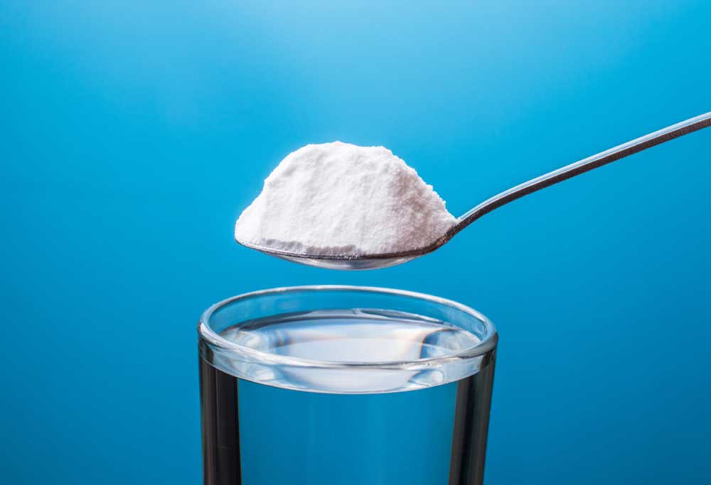 Baking soda on a spoon being held over a glass on water on a blue background