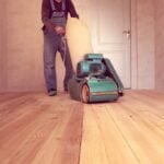 man using industrial sander to sand hardwood floors