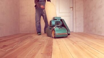 man using industrial sander to sand hardwood floors