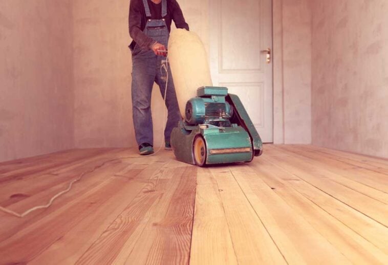 man using industrial sander to sand hardwood floors