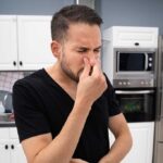 Man standing in the middle of his kitchen holding his nose