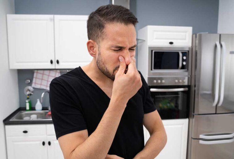 Man standing in the middle of his kitchen holding his nose
