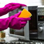 Pink gloved hands holding a sponge, opening a microwave as if to clean it