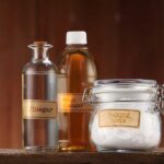 Bottles of vinegar and a glass jar of baking soda on a table with a dark wood background