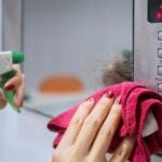 Hand holding rag and spray bottle, cleaning the front of a microwave