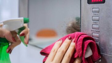 Hand holding rag and spray bottle, cleaning the front of a microwave