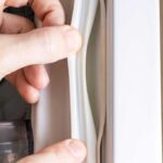 Fingers pulling back rubber door gasket from a fridge