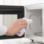 Hand holding white towel wiping out a microwave