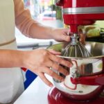 Person setting up whisk attachment on a red KitchenAid mixer