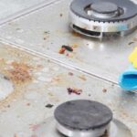 Gloved hand scrubbing a greasy, dirty, glass stove top.