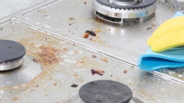 Gloved hand scrubbing a greasy, dirty, glass stove top.