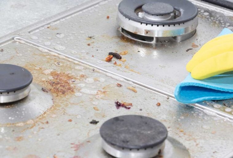 Gloved hand scrubbing a greasy, dirty, glass stove top.