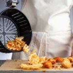 Chef pouring French fries from an air fryer basket onto a counter
