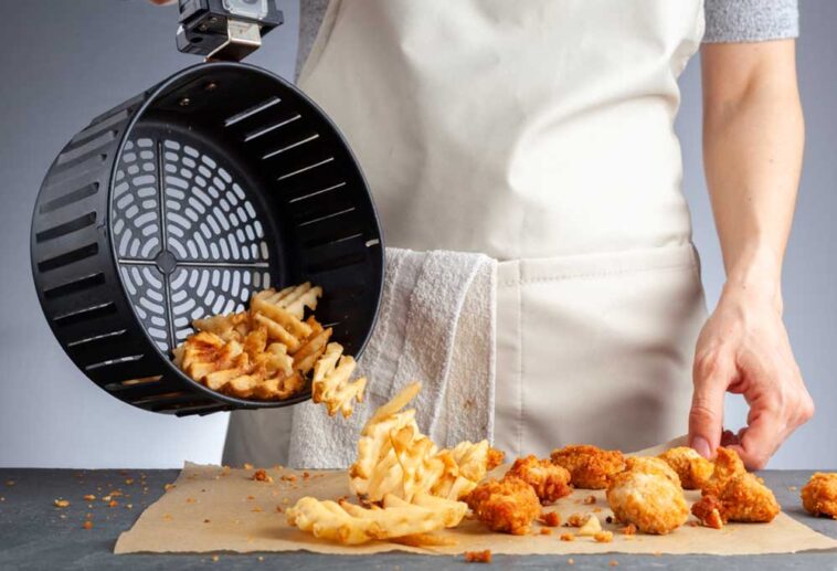 Chef pouring French fries from an air fryer basket onto a counter