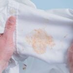 Hands stretching a white shirt to show an orange grease stain.