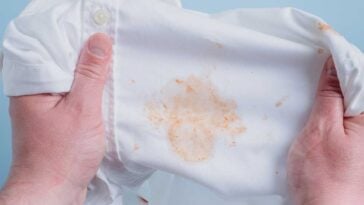 Hands stretching a white shirt to show an orange grease stain.