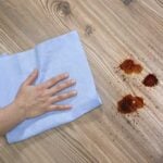 Hand on cloth, rubbing hardwood floor to remove grease
