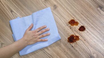 Hand on cloth, rubbing hardwood floor to remove grease