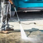 person pressure washing a brick paver driveway