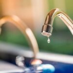 Close up of a dripping faucet in front of a window