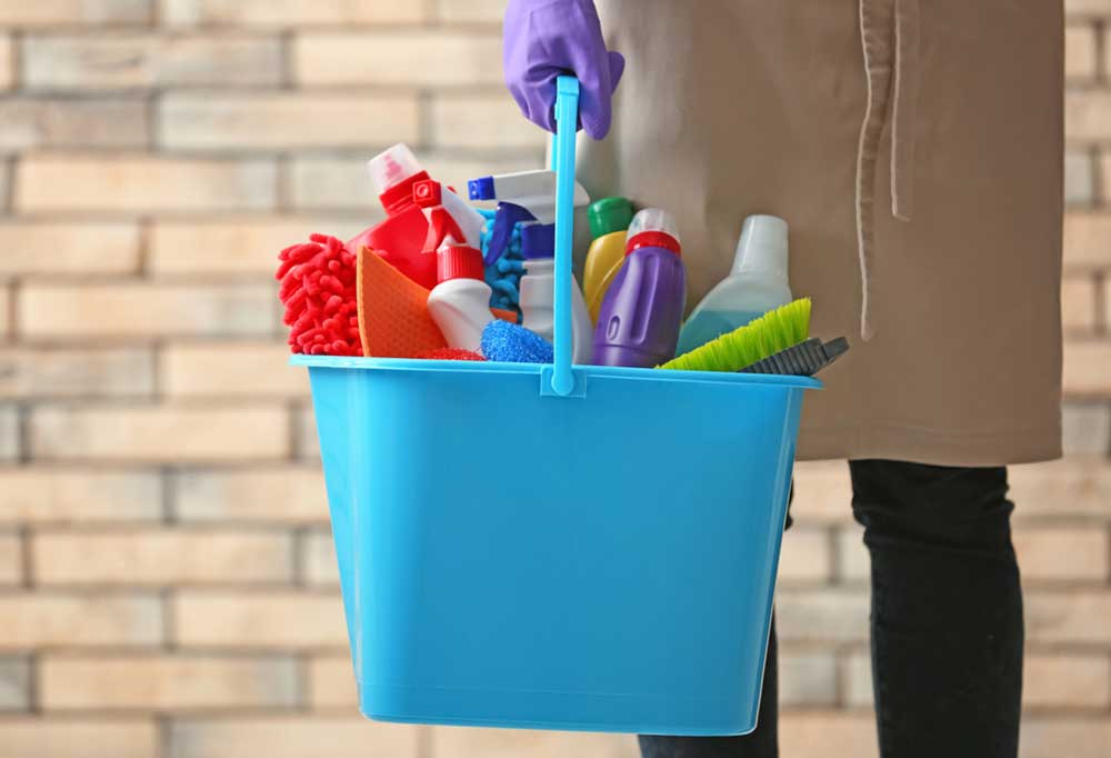 Bucket full of cleaning supplies being held by a purple gloved hand.